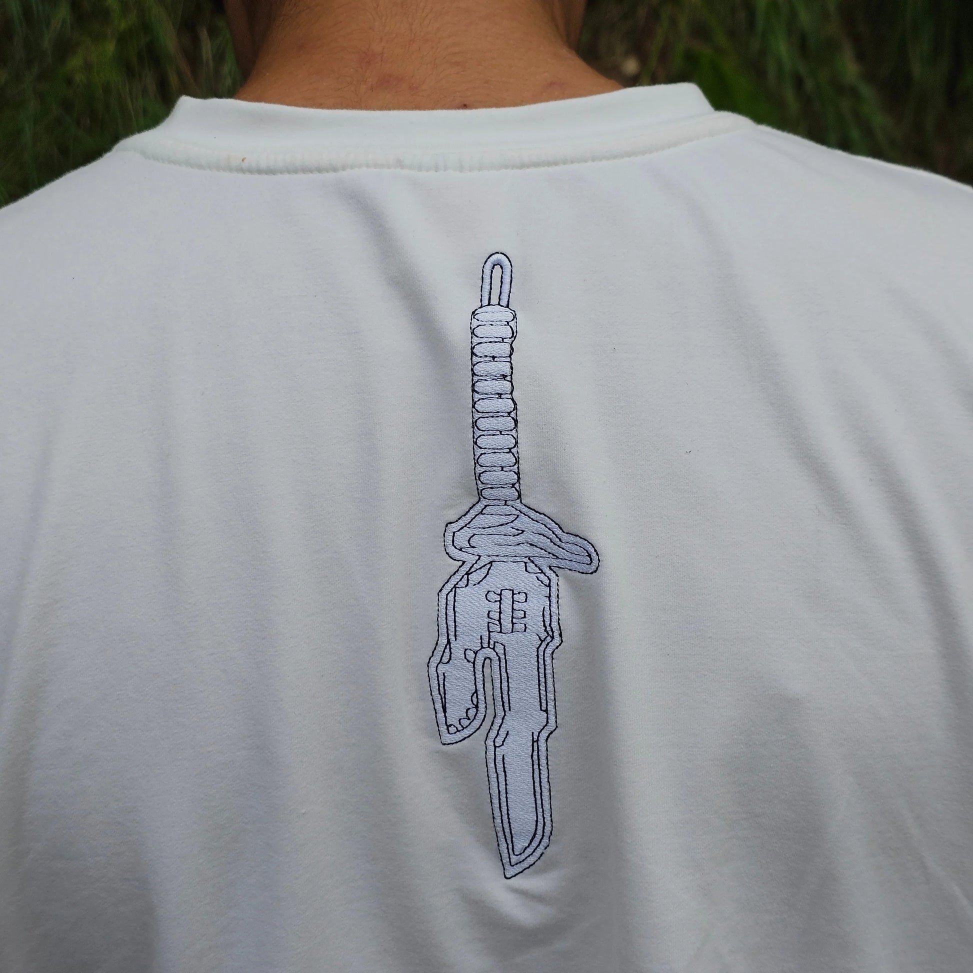 White shirt with a blue design on the back, person wearing it outdoors.