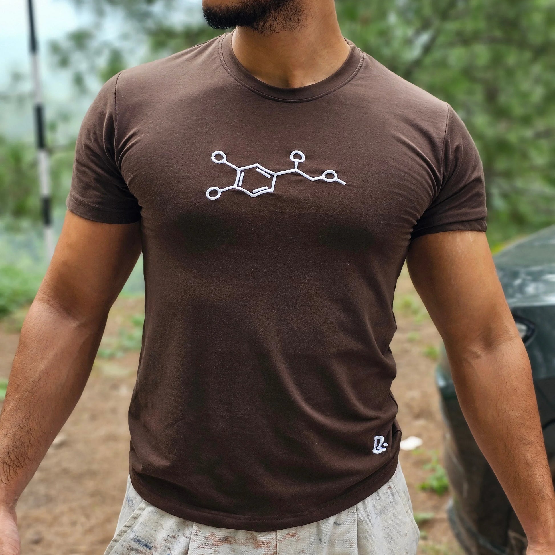 Man wearing a brown t-shirt with a white embrioder design outdoors