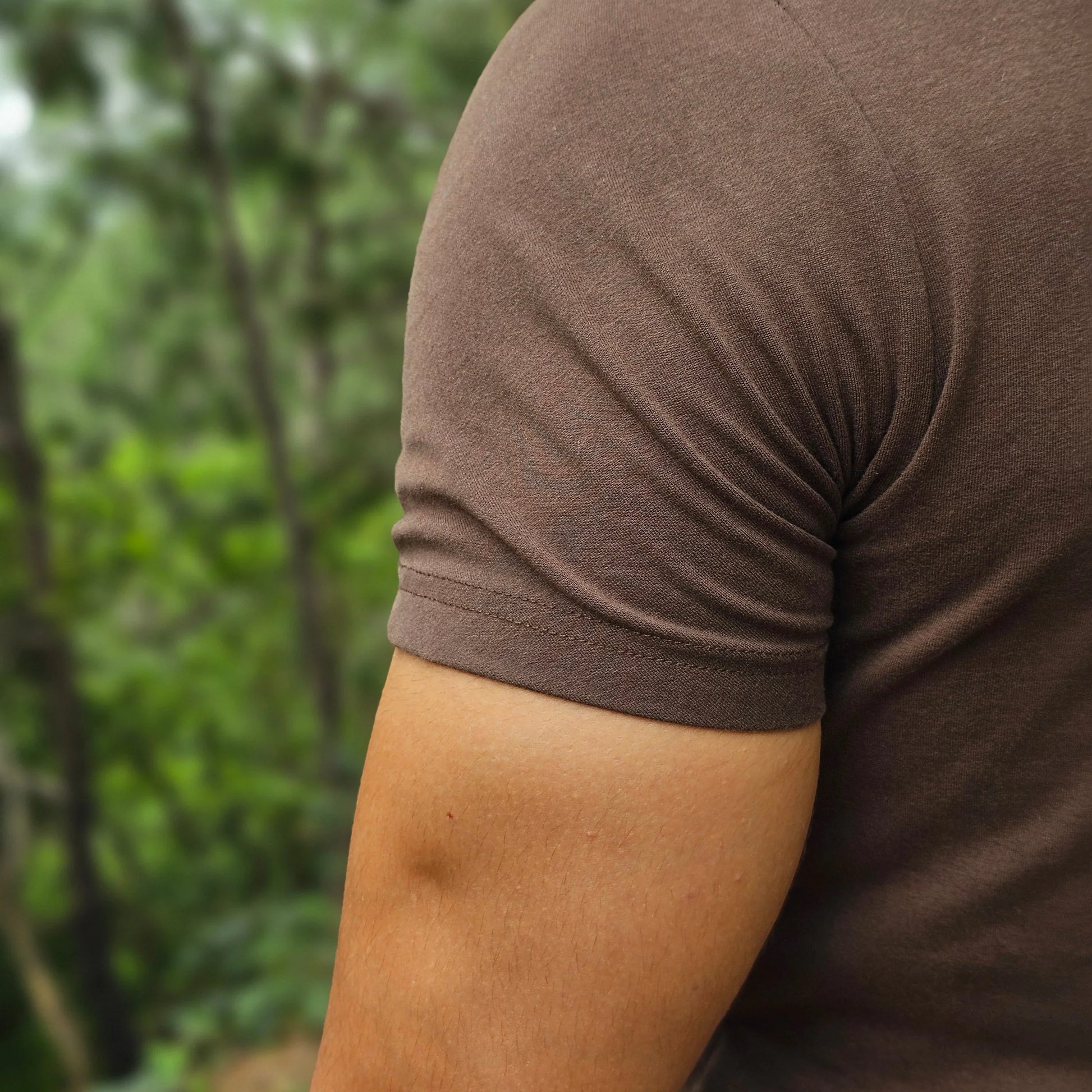 Close-up of a person wearing a brown long-sleeve shirt with a blurred green background
