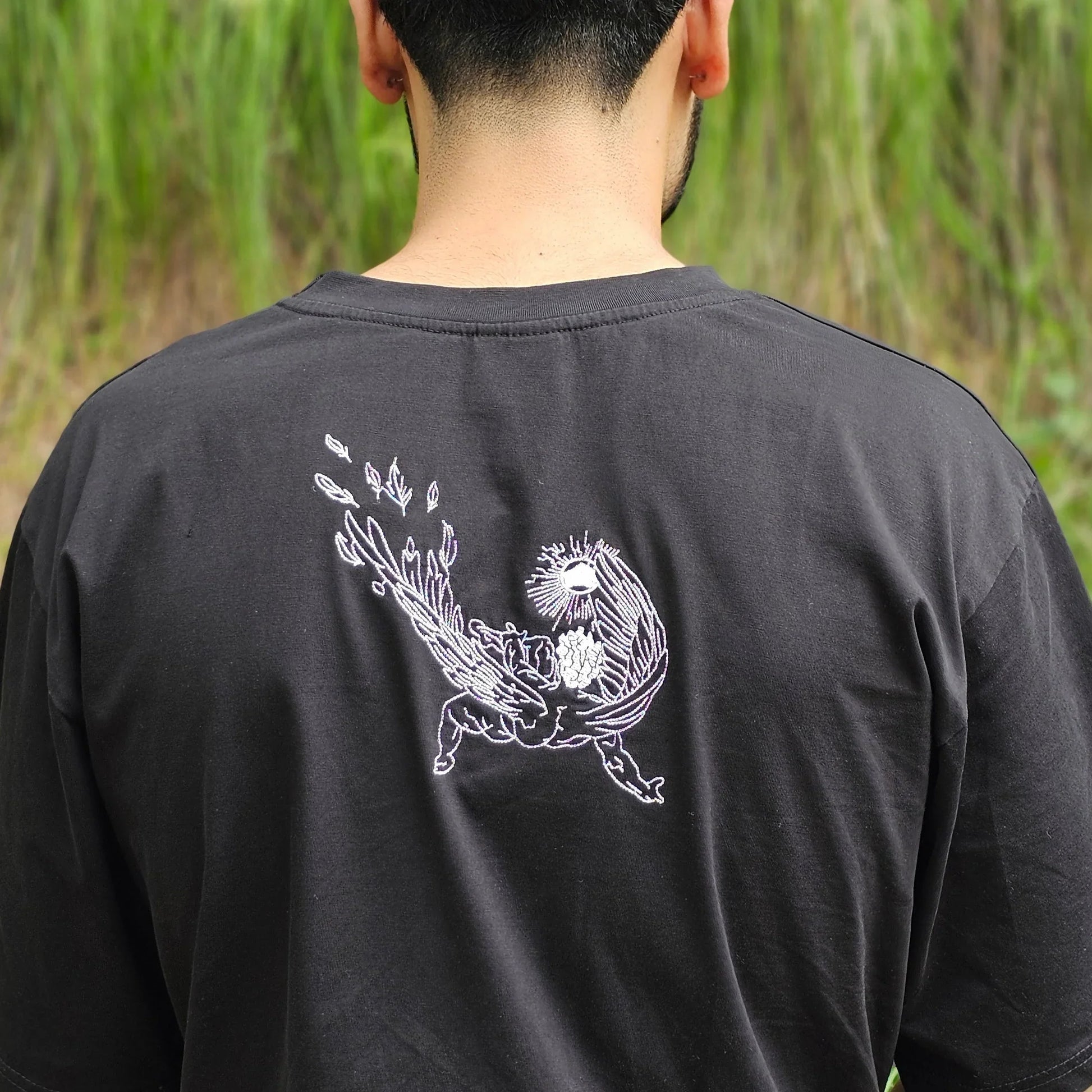 Person wearing a black long-sleeve shirt with a white graphic on the back, standing in a grassy area.