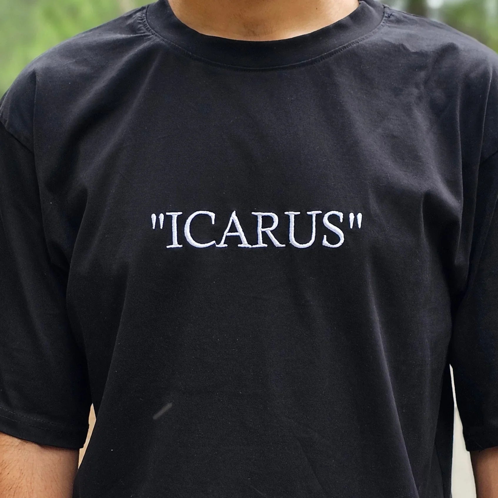 Person wearing a black t-shirt with 'ICARUS' text outdoors.