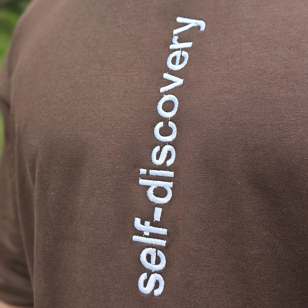Brown fabric with 'self-discovery' embroidered in white on a blurred green background
