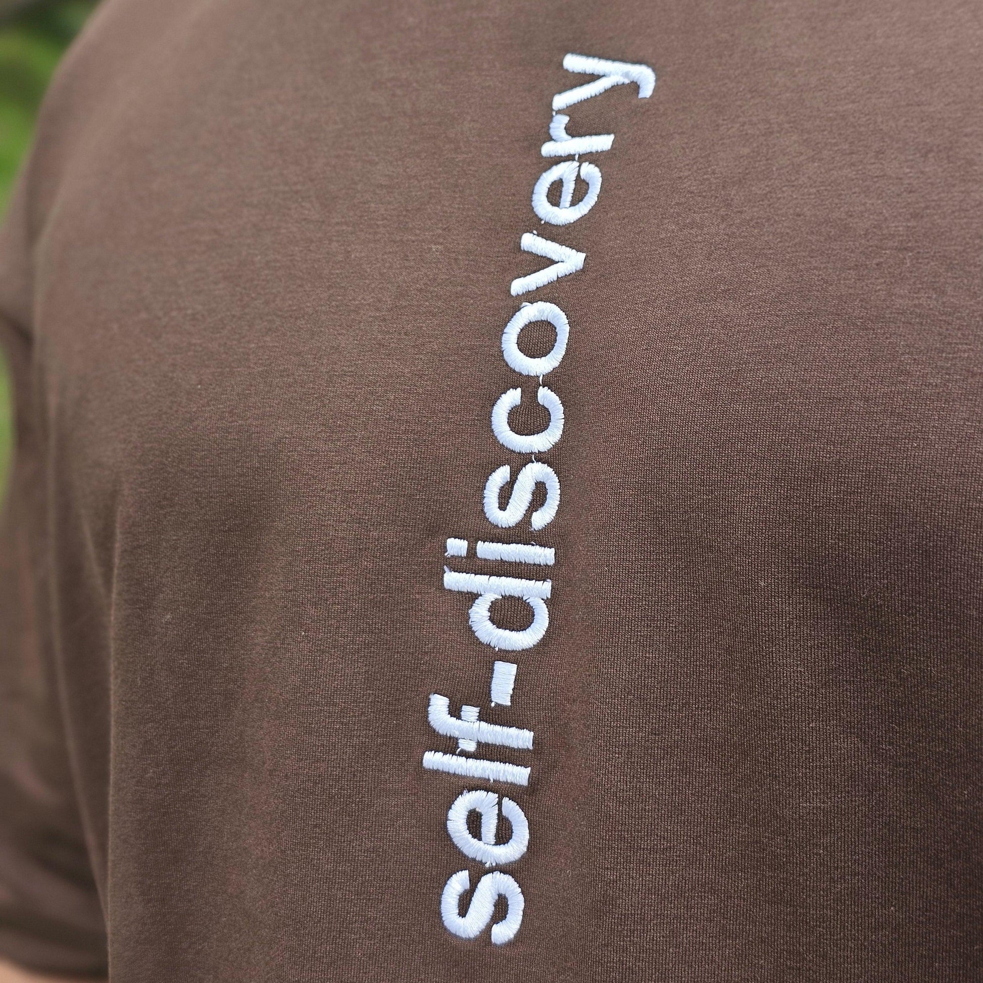 Brown fabric with 'self-discovery' embroidered in white on a blurred green background