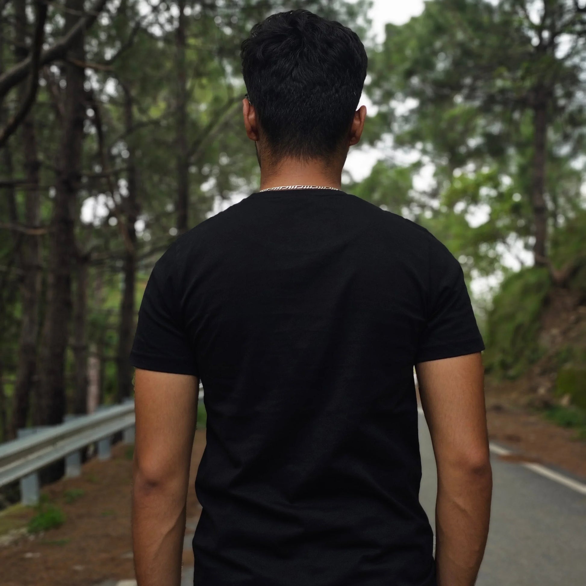 Person in a black t-shirt standing outdoors with trees in the background
