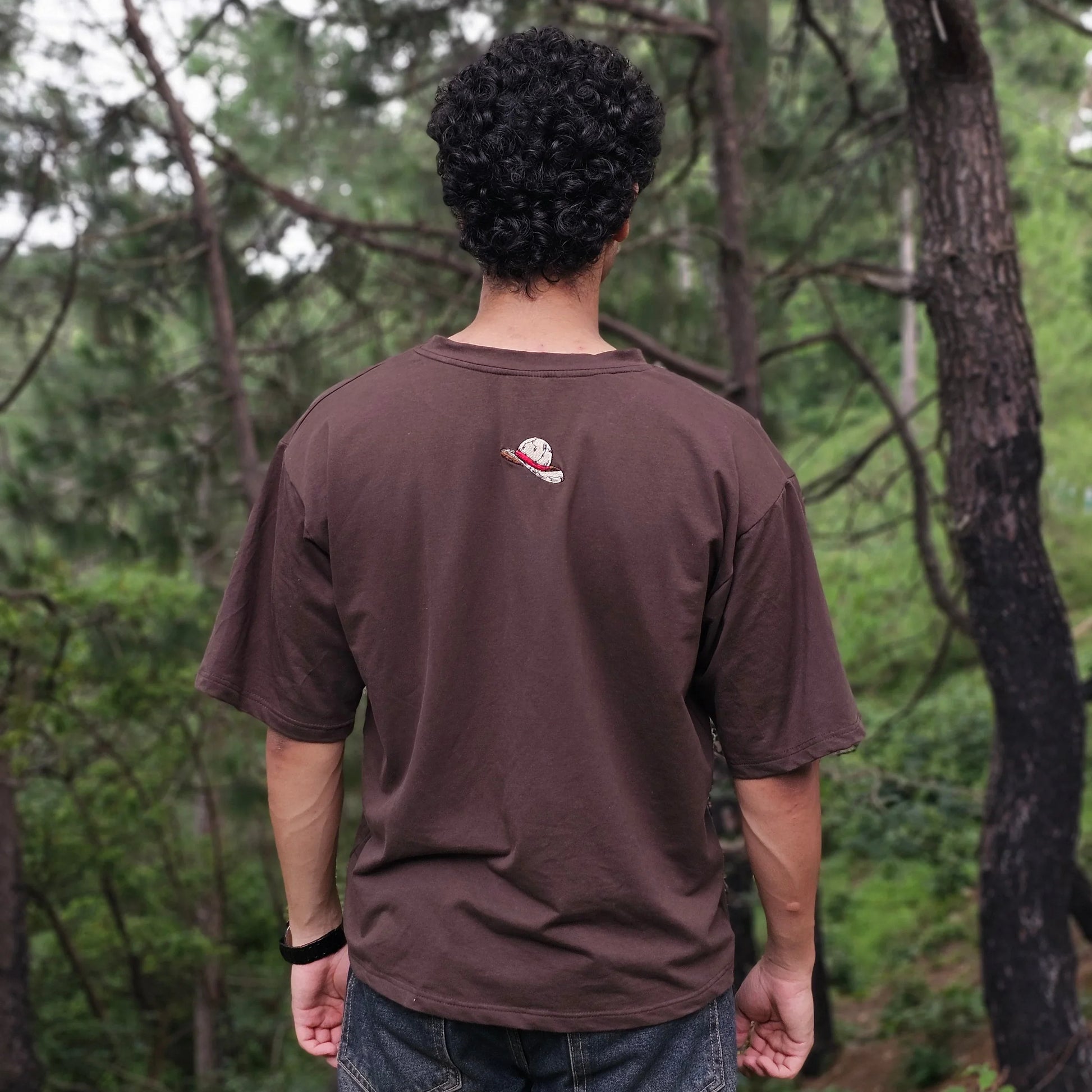 Person wearing a brown sweatshirt with a logo in a forest setting