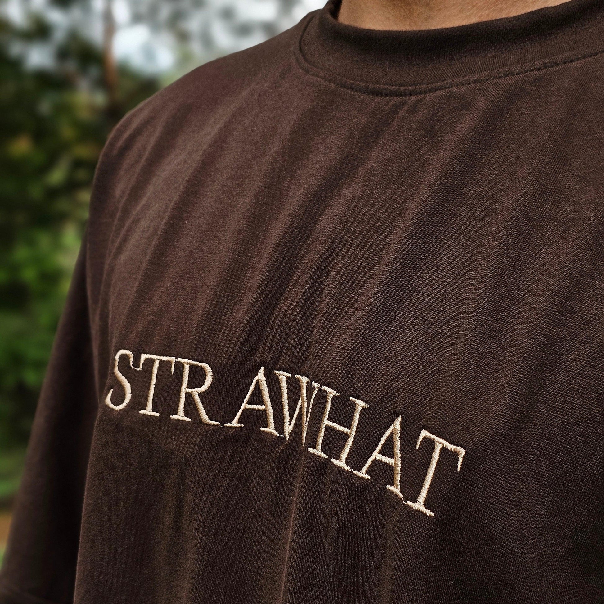 Brown sleeveless shirt with 'STRAWHAT' logo on a blurred natural background