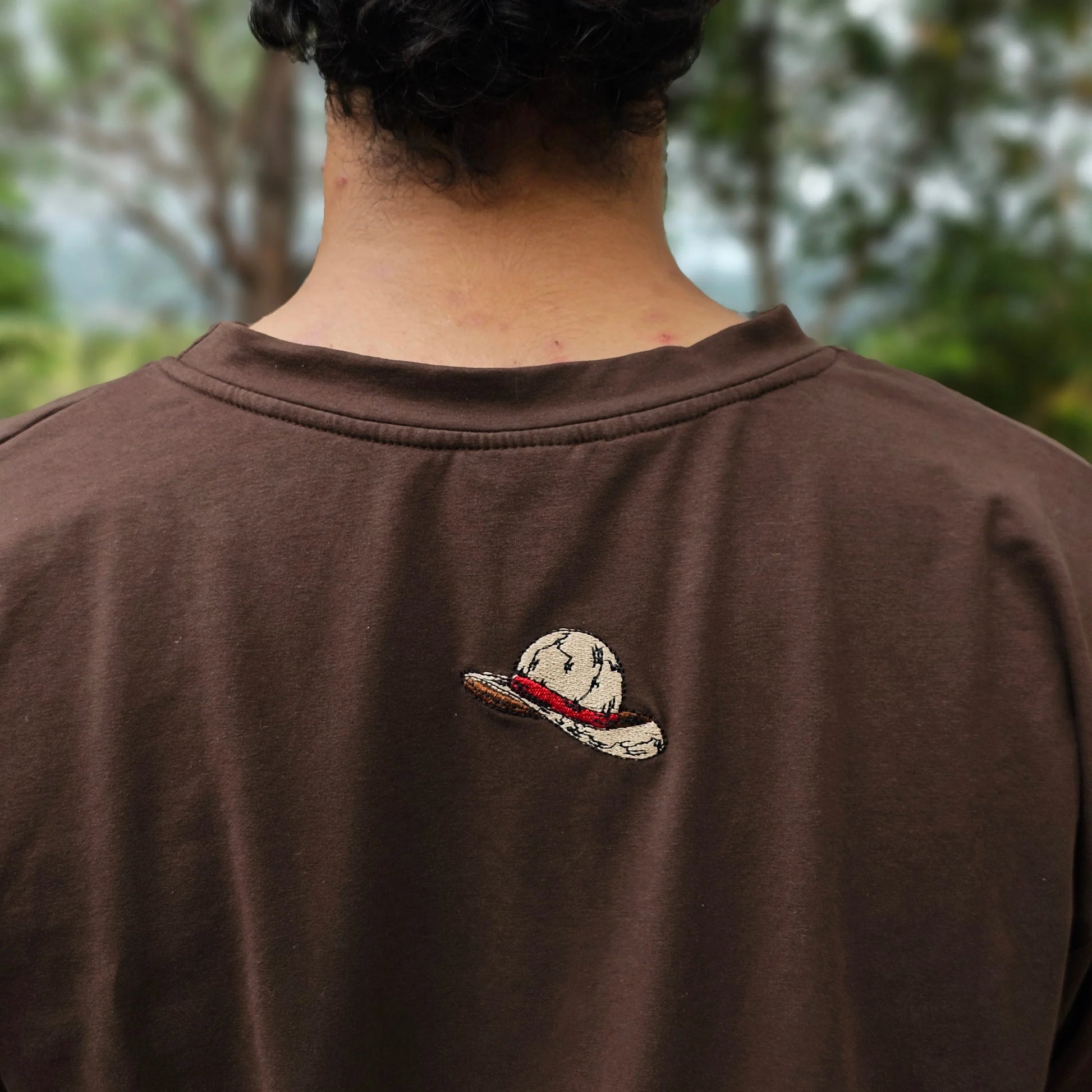 Brown shirt with a Anime Cap design on the Back embrioded against a blurred natural background