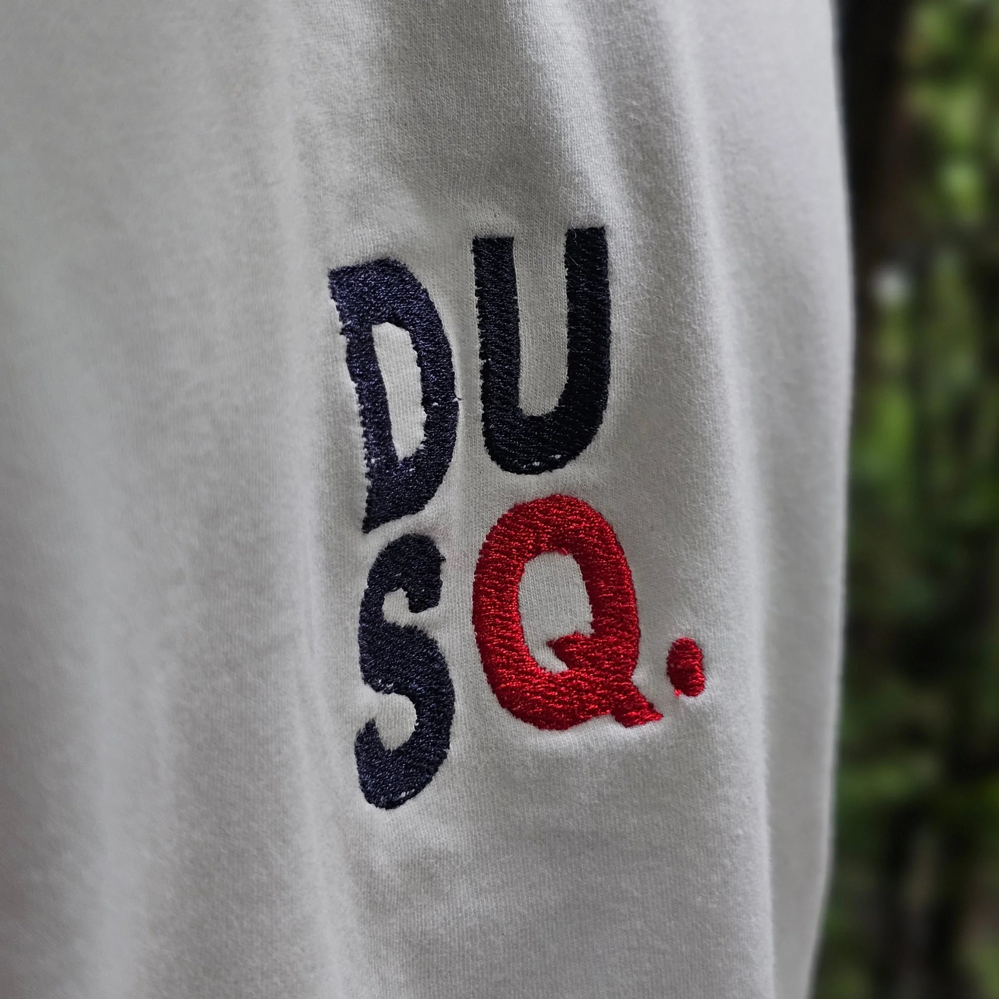 Embroidered logo on a white fabric background with blurred greenery in the background