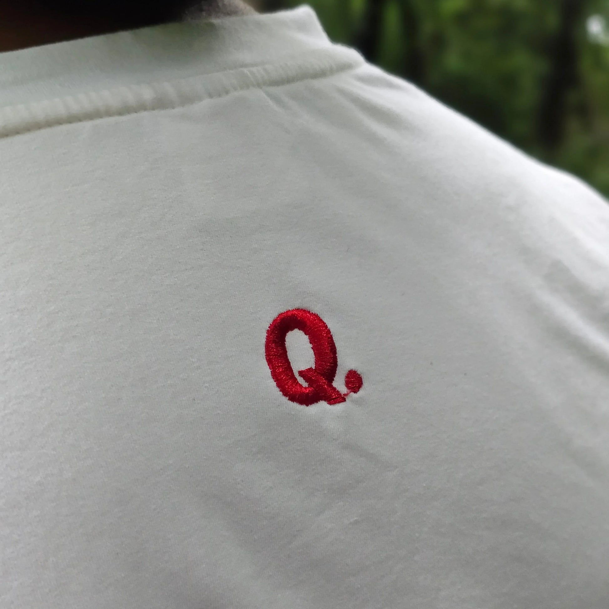 White shirt with a red embroidered logo on a blurred green background