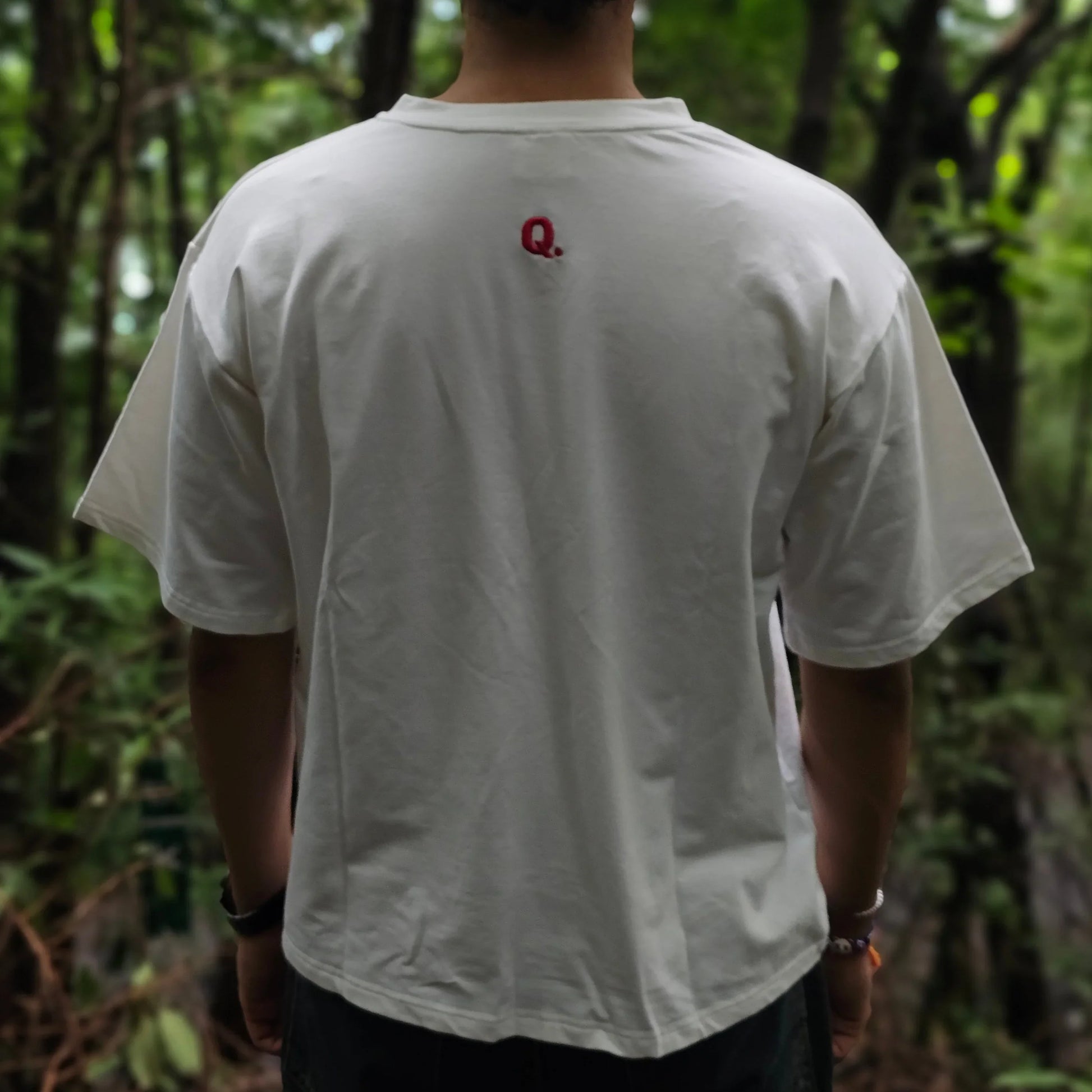 Person wearing a white shirt with a red logo in a forest setting