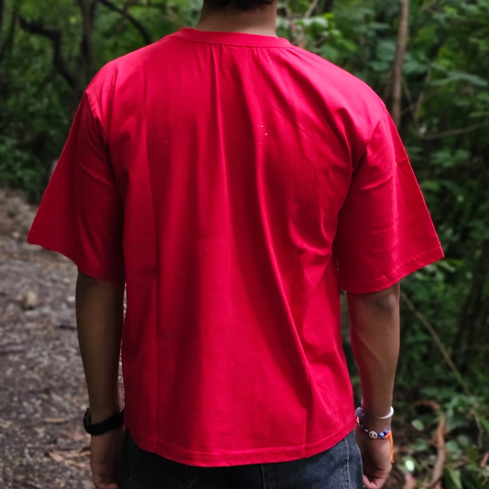 Person wearing a red shirt standing outdoors with trees in the background