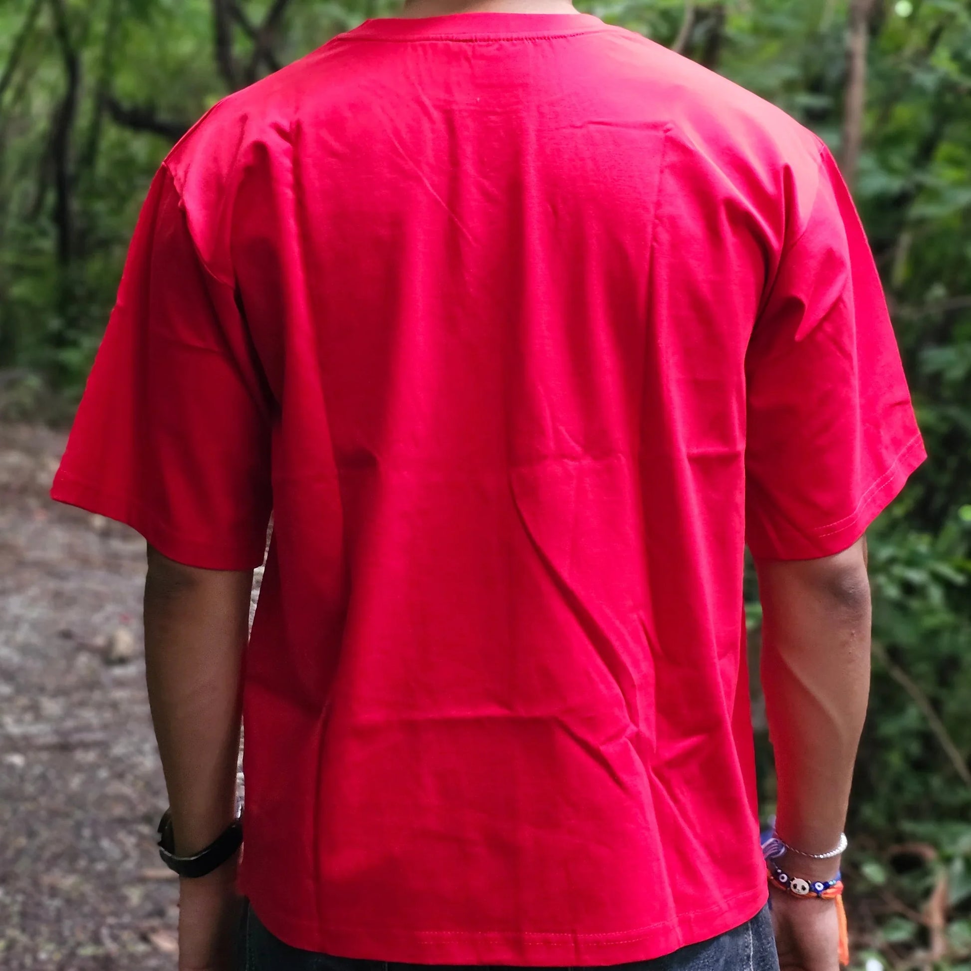 Person wearing a red shirt standing outdoors with trees in the background