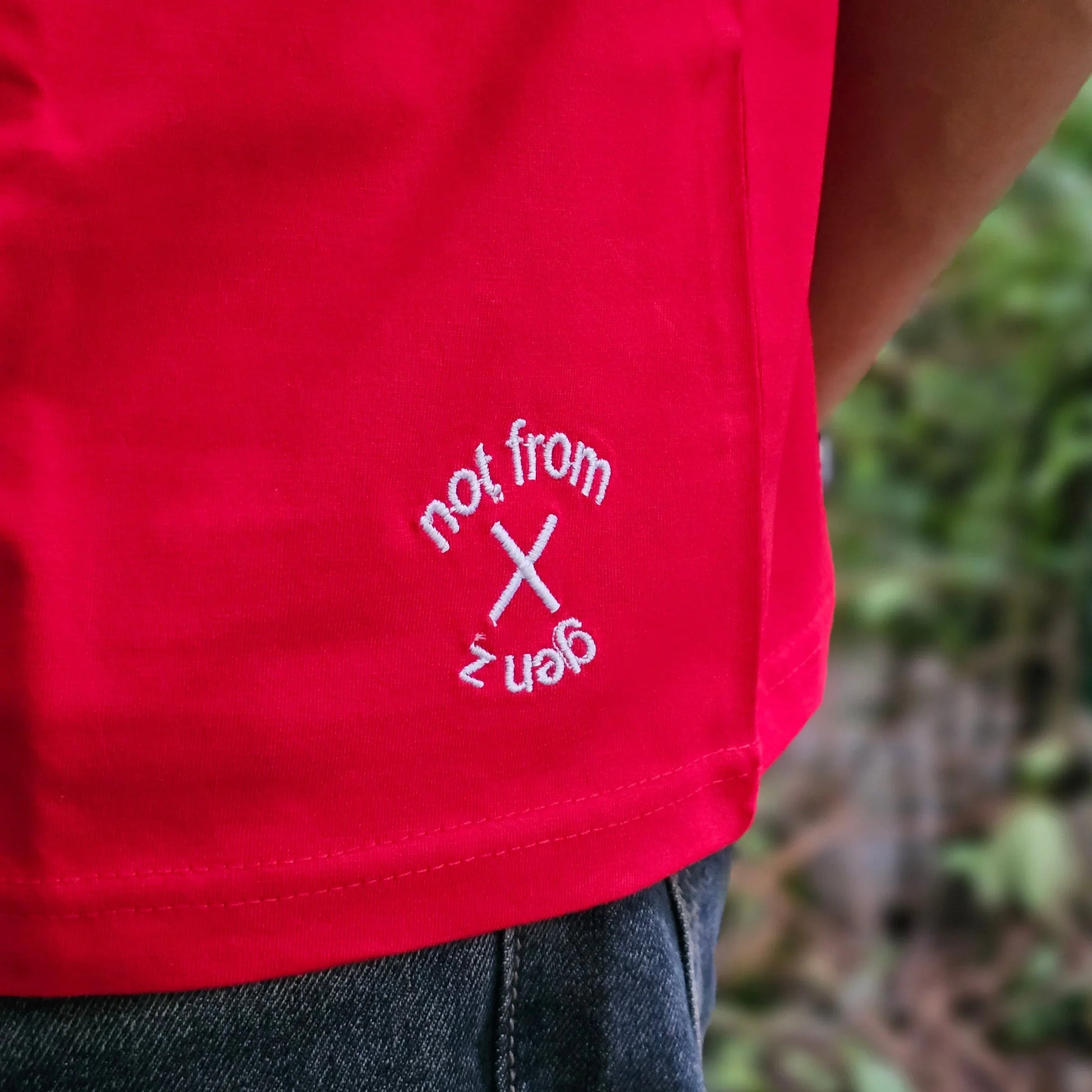 Red shirt with white text and logo worn by a person, with a blurred green background