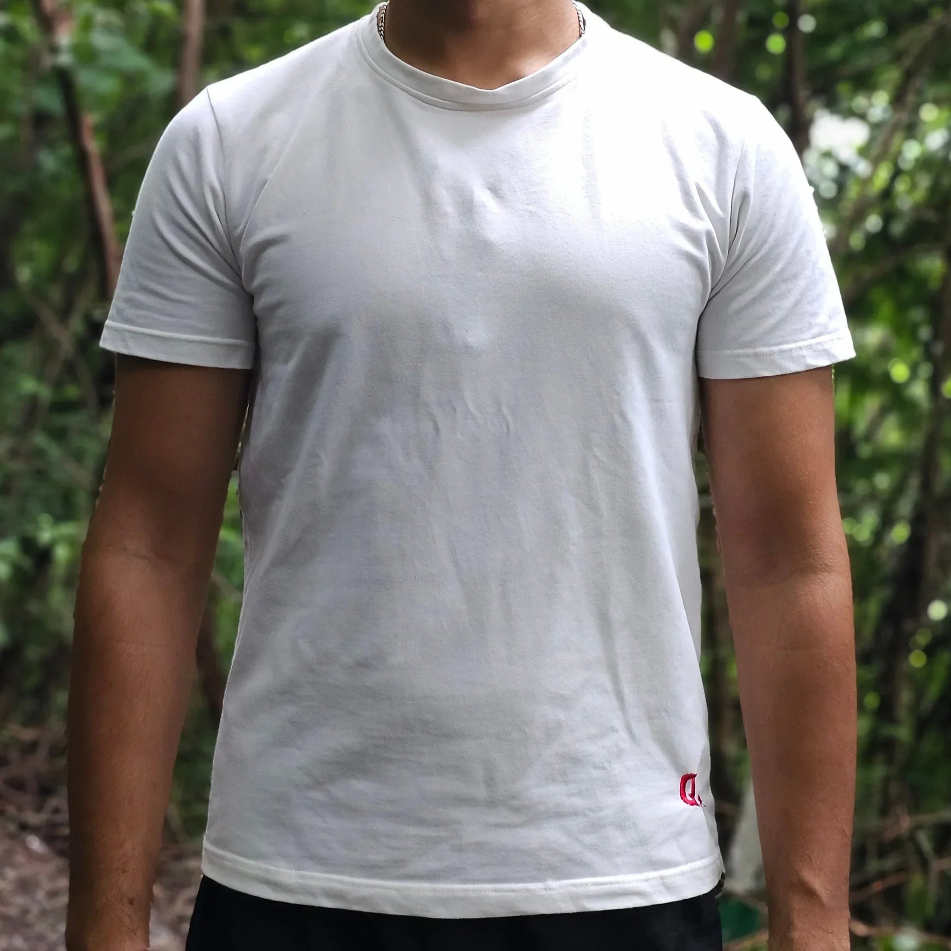Man wearing a white t-shirt standing outdoors with greenery in the background