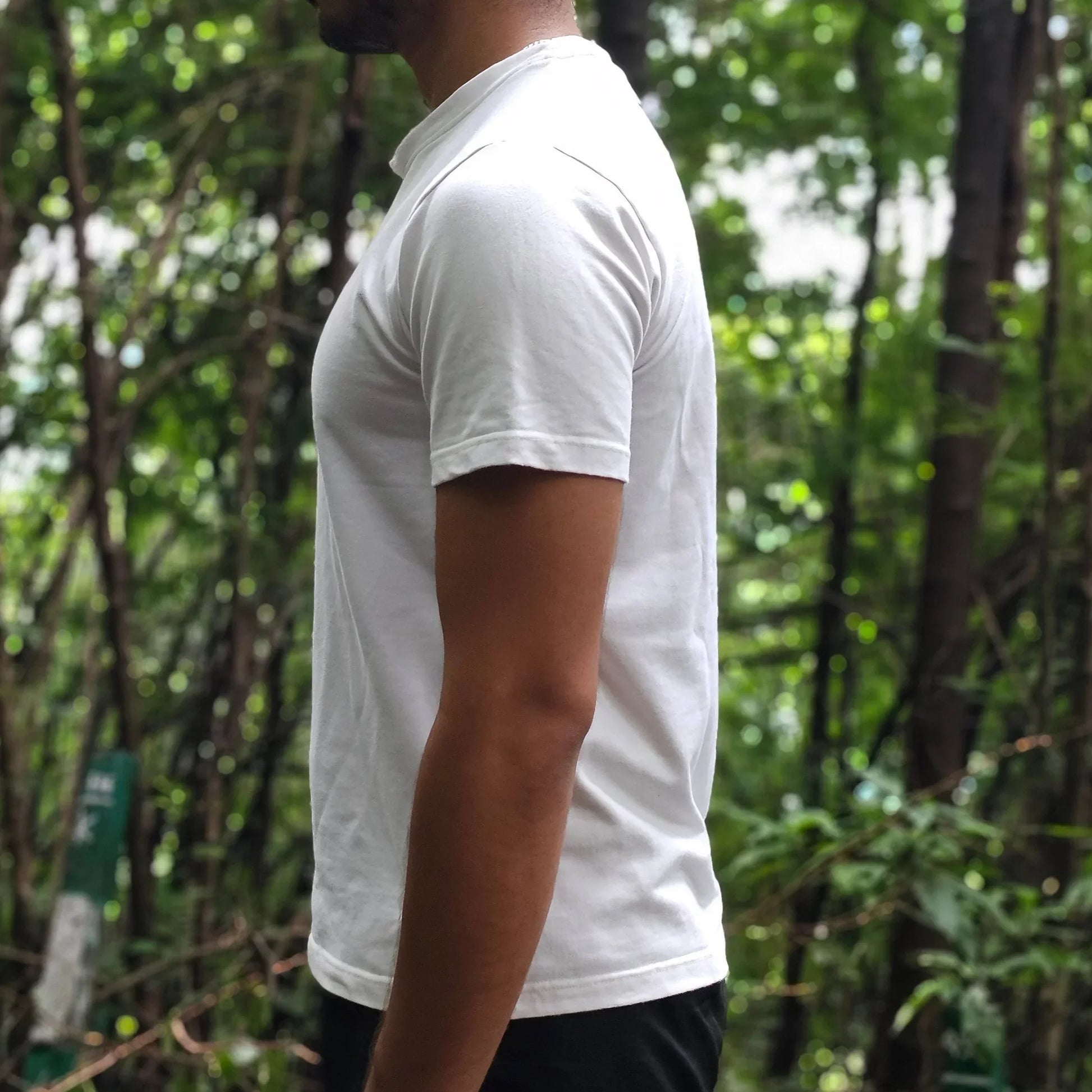 Person in a white shirt and black shorts standing outdoors with trees in the background