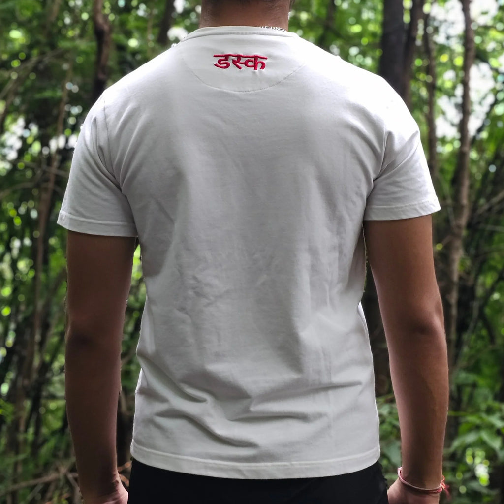 Person wearing a white t-shirt with a logo, standing outdoors with trees in the background