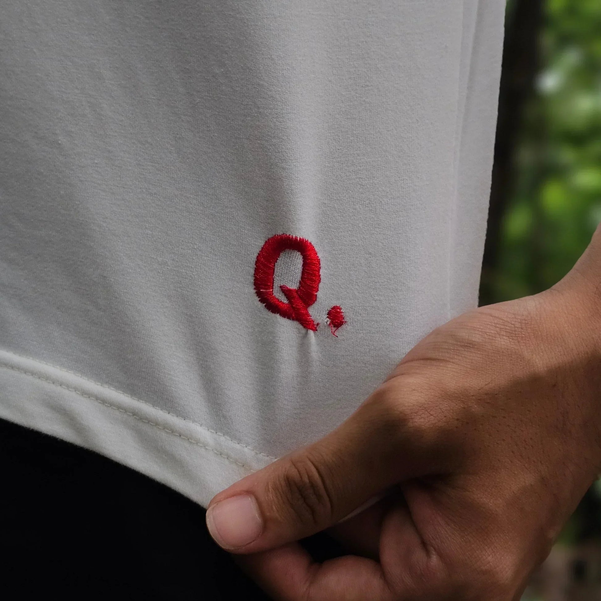 White fabric with a red Q embroider held by a hand against a blurred green background