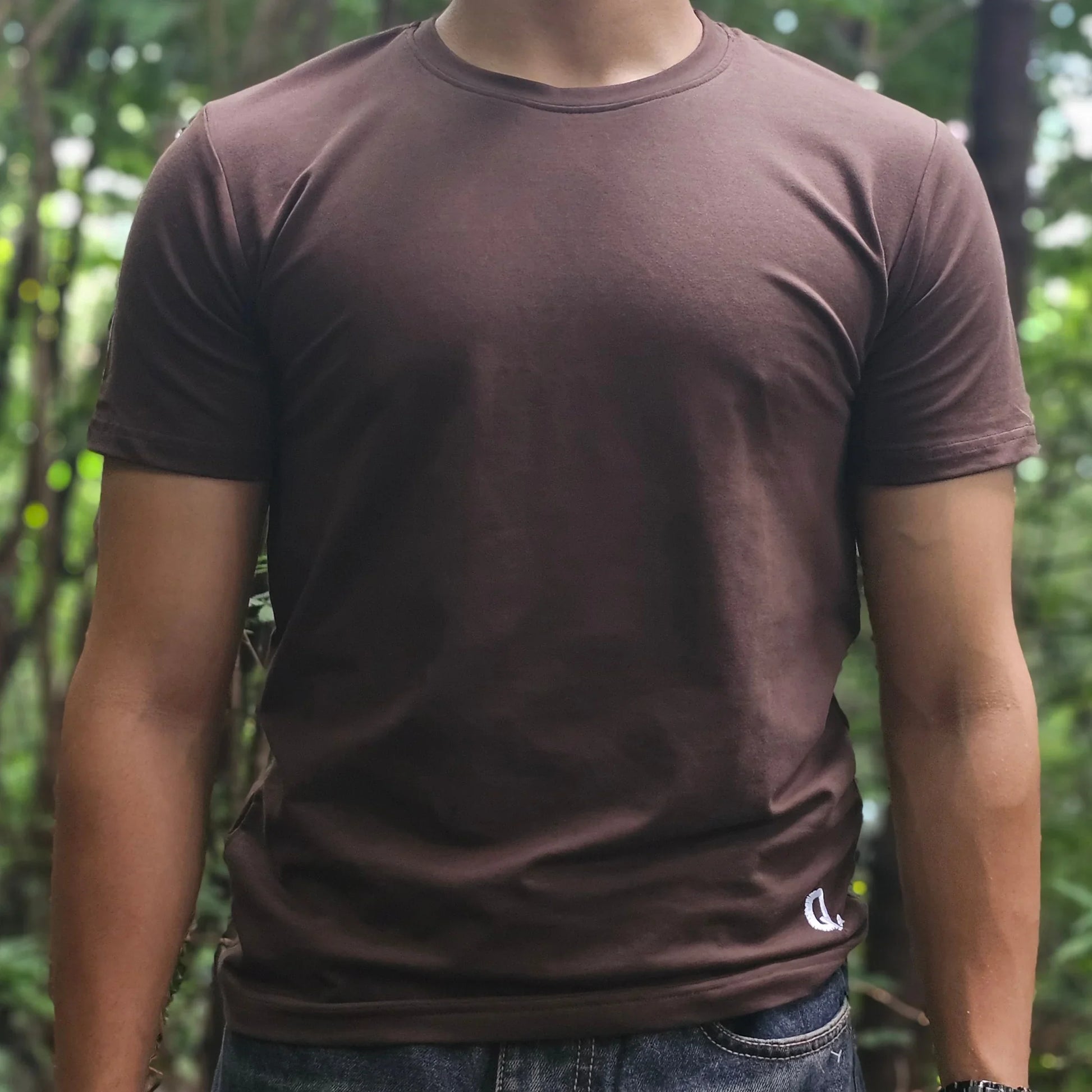 Person wearing a brown shirt and jeans standing in a forest
