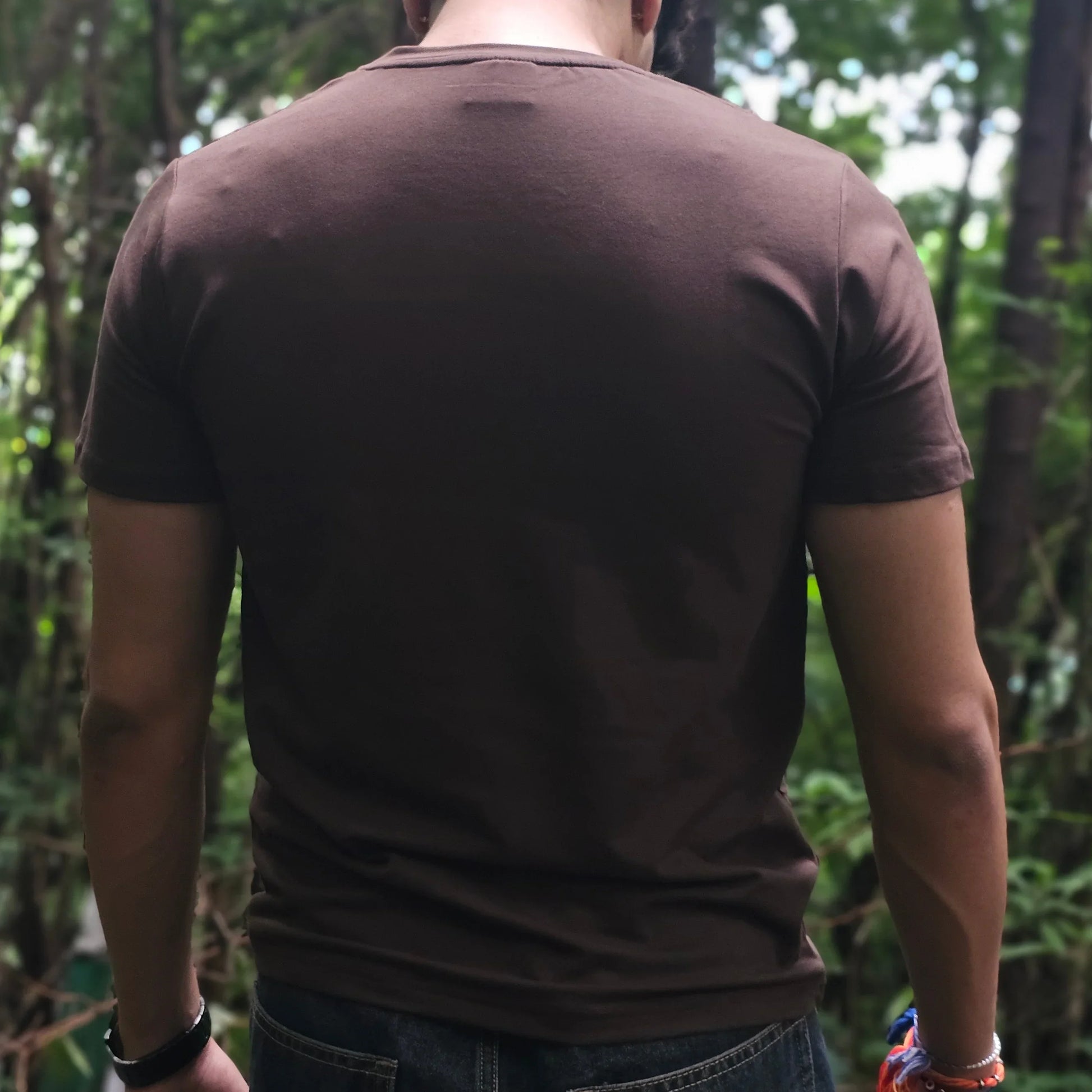 Person wearing a brown shirt and jeans standing in a forest