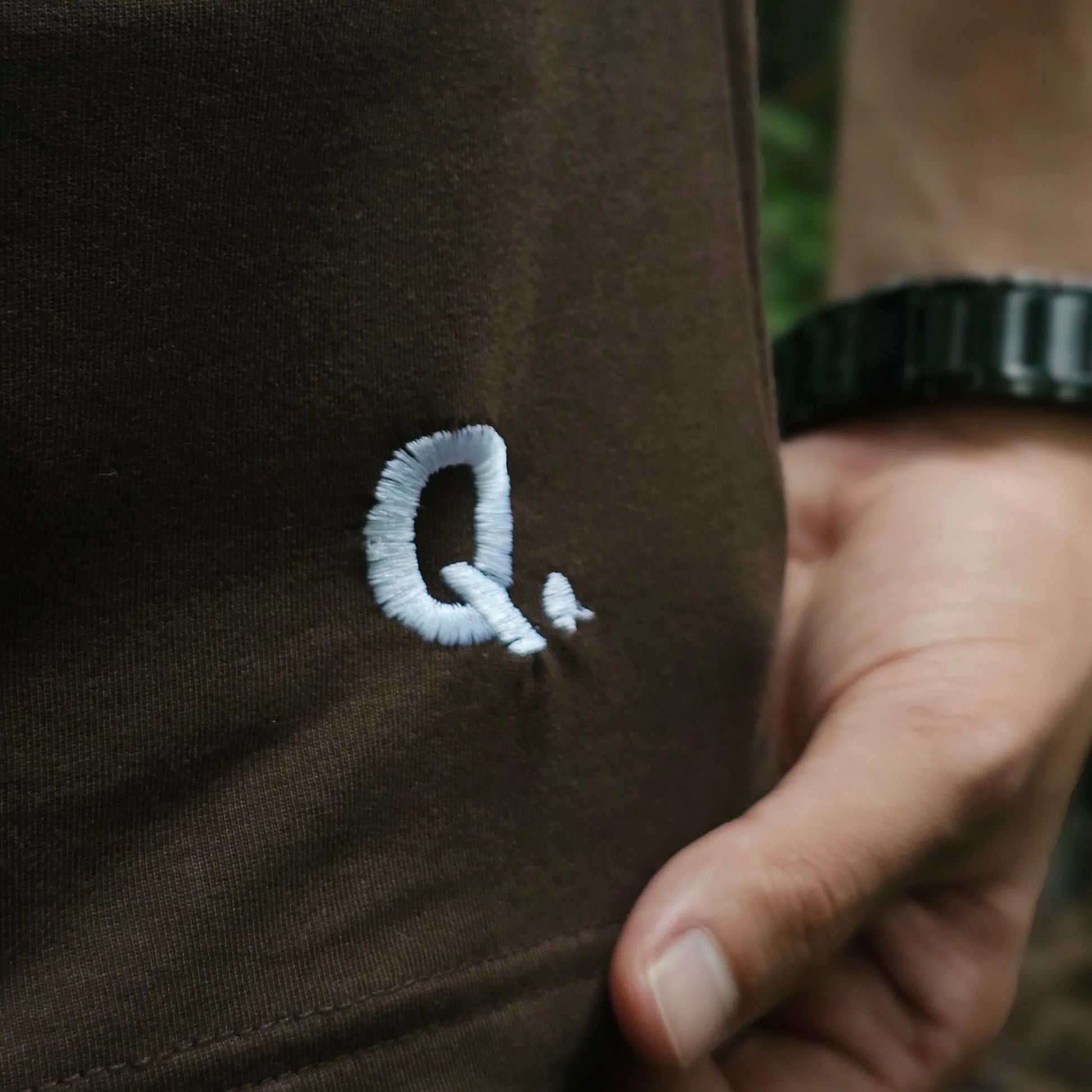 Close-up of a white embroidered design on a brown fabric surface.